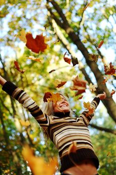 woman drop up leaves in autumn park