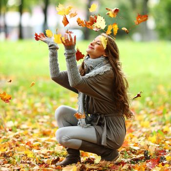 woman drop up leaves in autumn park