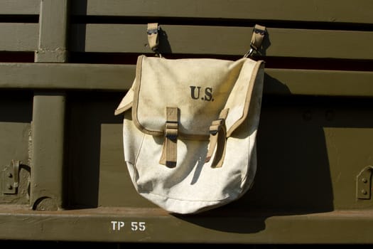 A vintage world war 2 American satchel, kit bag, with a U.S. label attached to an olive green vehicle.