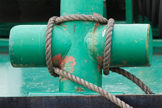 Painted green cross-shaped marine bollard with a ships hawser wound round it for mooring in a port or harbour