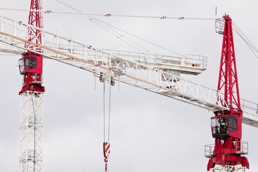 Detail of two large steel construction cranes with red operator cabs for hoisting heavy loads during building construction and development