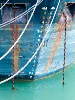Closeup of the bow hull with floatation depth scale gauge of a ship with grungy rust streaks from corroded anchor chains