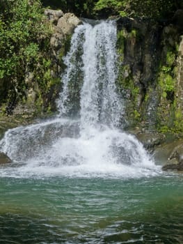 Natural waterfall casdcading over rocks into a calm blue pond below