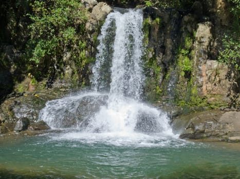 Natural waterfall casdcading over rocks into a calm blue pond below
