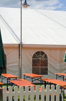 A white party or event tent with beer tables and benches and lantern