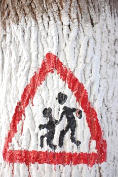 Warning road sign drawn on a tree trunk.
Attention children.