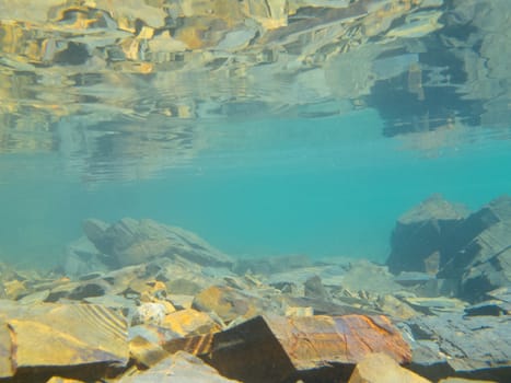 Underwater shot in shallow water over submerged rocks with reflection of rocky bottom from underneath calm surface