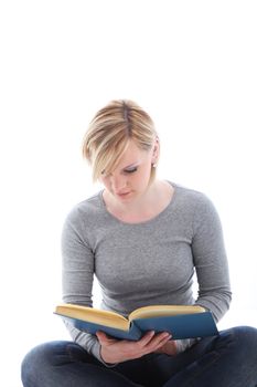 Young female student sitting cross legged on the floor stydying from a textbook isolated on white 