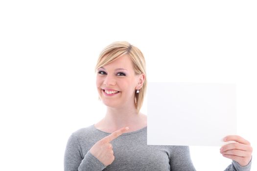 Smiling woman pointing with her finger to a blank sign that she is holding up to the side of her face isolated on white 