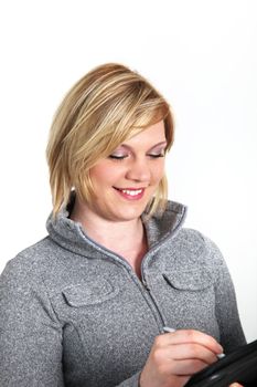 Pretty smiling young blonde woman in a grey winter top writing notes in a handheld file 