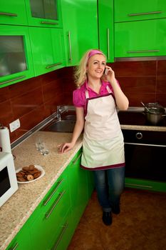 A young housewife, speaks on a cell phone in the kitchen