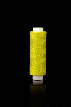 Yellow spindle of yarn isolated over black background