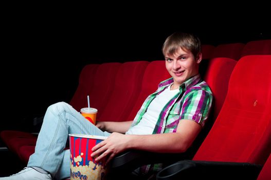 man in a movie theater, watching a movie and drink a drink