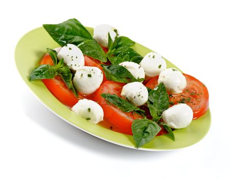 Italian Caprese Salad with Basil, Fresh Mozzarella, Tomatoes and Olive Oil on green plate isolated on white background