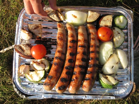 Hands on a disposable barbecue with sausages, onions and vegetables
