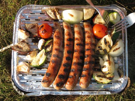 Disposable barbecue with sausages, vegetables, onions and cutlery