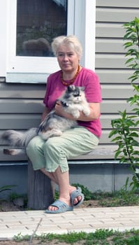 Woman sits on summer residence with thoroughbred cat on hands