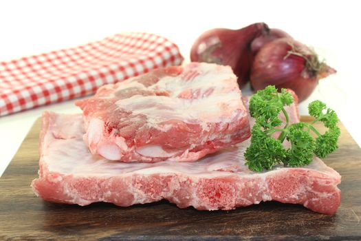 Beef spare ribs with parsley and onions on a wooden board in front of light background