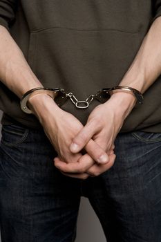 Unreconizable teenager with handcuffs on grey background