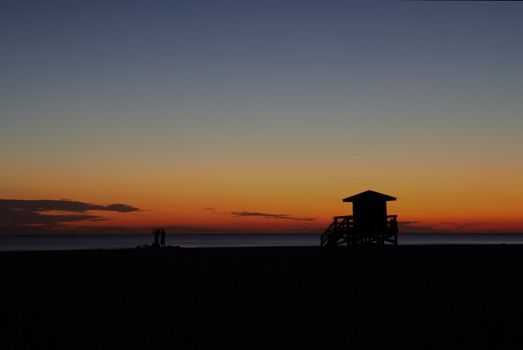 HDR image of a lifeguard station on Siesta Key Beach, Florida silhouetted against the setting sun with a dark blue and orange sky
