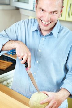 Happy man in kitchen holding knife to cut melon