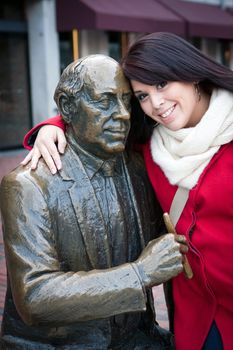 Young woman puts her arm around the public Red Auerbach statue found in Bostons Quincy Market just outside of Faneuil Hall.