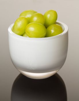 White glass cup full of green grapes reflecting on shiny gradient surface