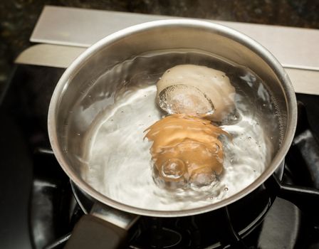 Two eggs in boiling water in stainless steel pan on gas hob