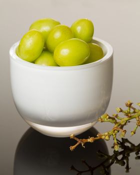 White glass cup full of green grapes reflecting on shiny gradient surface
