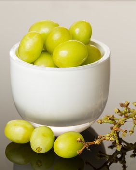 White glass cup full of green grapes reflecting on shiny gradient surface