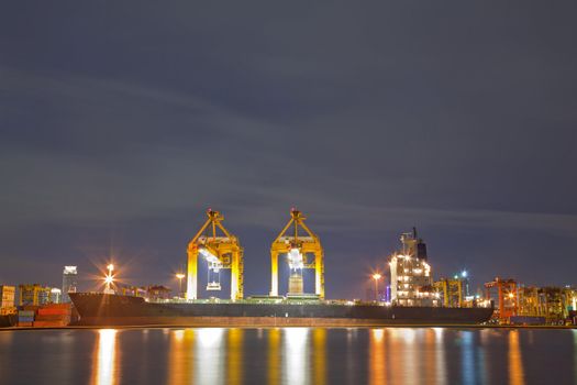 Industrial Container Cargo freight ship with working crane bridge in shipyard at dusk for Logistic Import Export background