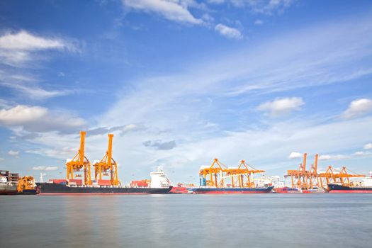 Cargo Ships Loading and unloading goods container with cranes at Port Terminal with beautiful cloudscape for heavy industry and logistic background