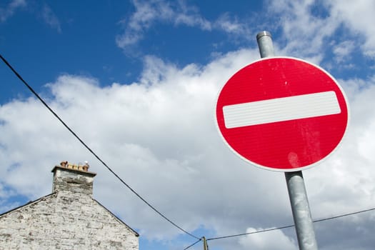 A no entry sign with a red circle and white bar on a metal post against a blue sky with cloud.