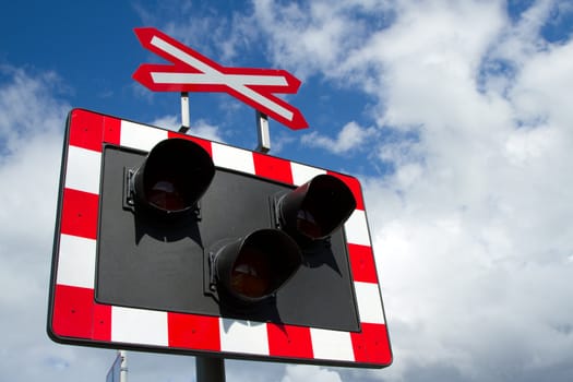 The red and white warning symbols with a cross on top of a metal board with three lights against a blue sky with cloud.