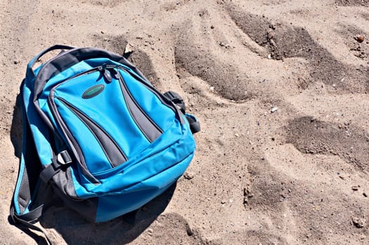 Backpack of blue color on a sandy beach.