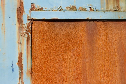 A rusty metal sheet with a half frame of blue damaged flaking paint.