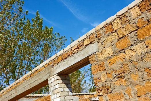 Construction of the house with a hollow limestone blocks on the background of trees and blue sky