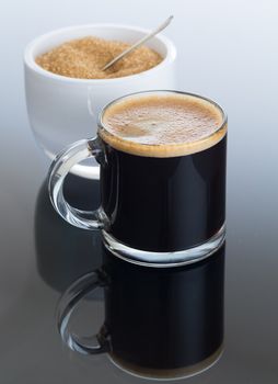 Black expresso coffee in small glass cup with sugar in white bowl reflecting