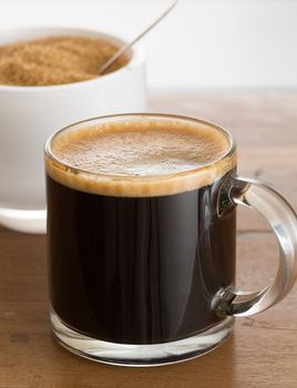 Black expresso coffee in small glass cup with sugar in white bowl reflecting
