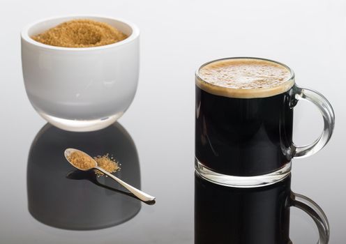 Black expresso coffee in small glass cup with sugar in white bowl reflecting