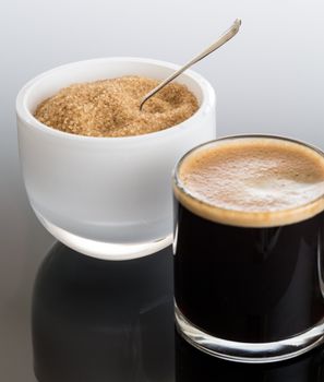 Black expresso coffee in small glass cup with sugar in white bowl reflecting