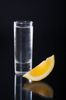 Shot glass filled with clear alcohol on a black background