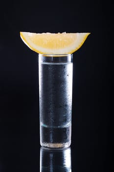 Shot glass filled with clear alcohol on a black background