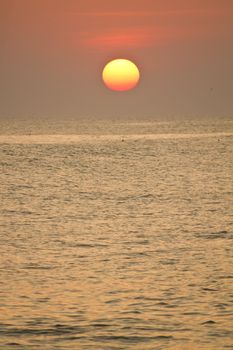 View of a big red sun at sunset on a calm beach.