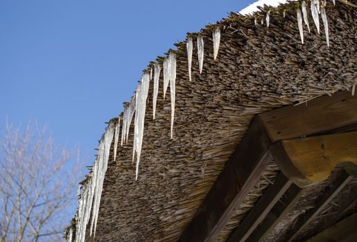 small icicles on retro straw roof on background of dark blue sky in winter.