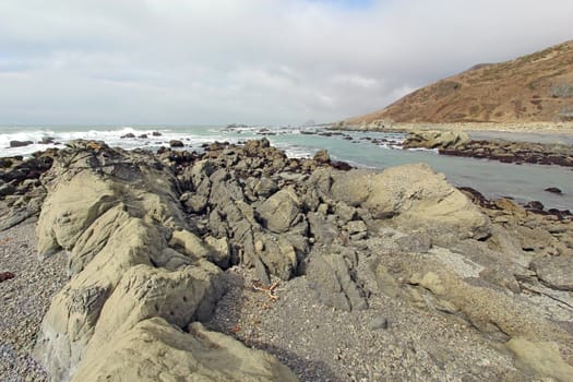 A rocky beach off of Mattole Road on the Lost Coast of California with breaking surf and a cloudy sky
