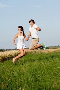 young happy couple jumping outside in summer on field 