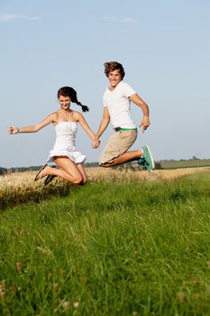 young happy couple jumping outside in summer on field 