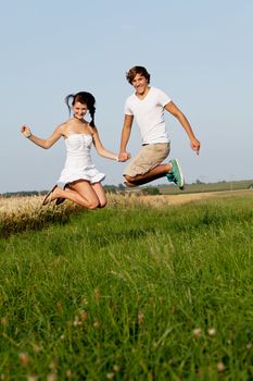 young happy couple jumping outside in summer on field 