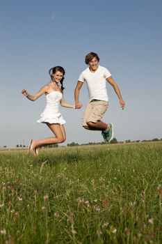 young happy couple jumping outside in summer on field 